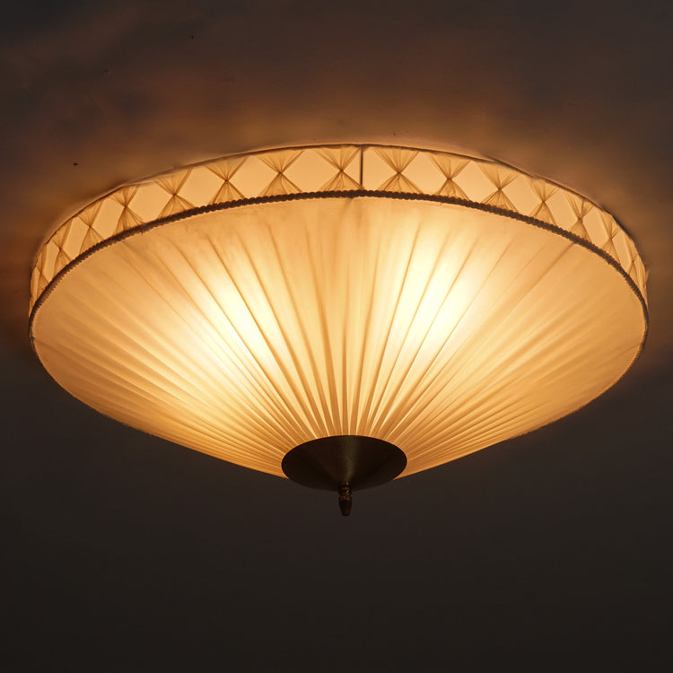Round flush mount. A natural white plastic shade.The edge of the shade is surrounded by a detail with the same white fabric in vertical bows. In the centre, a circular brass detail.