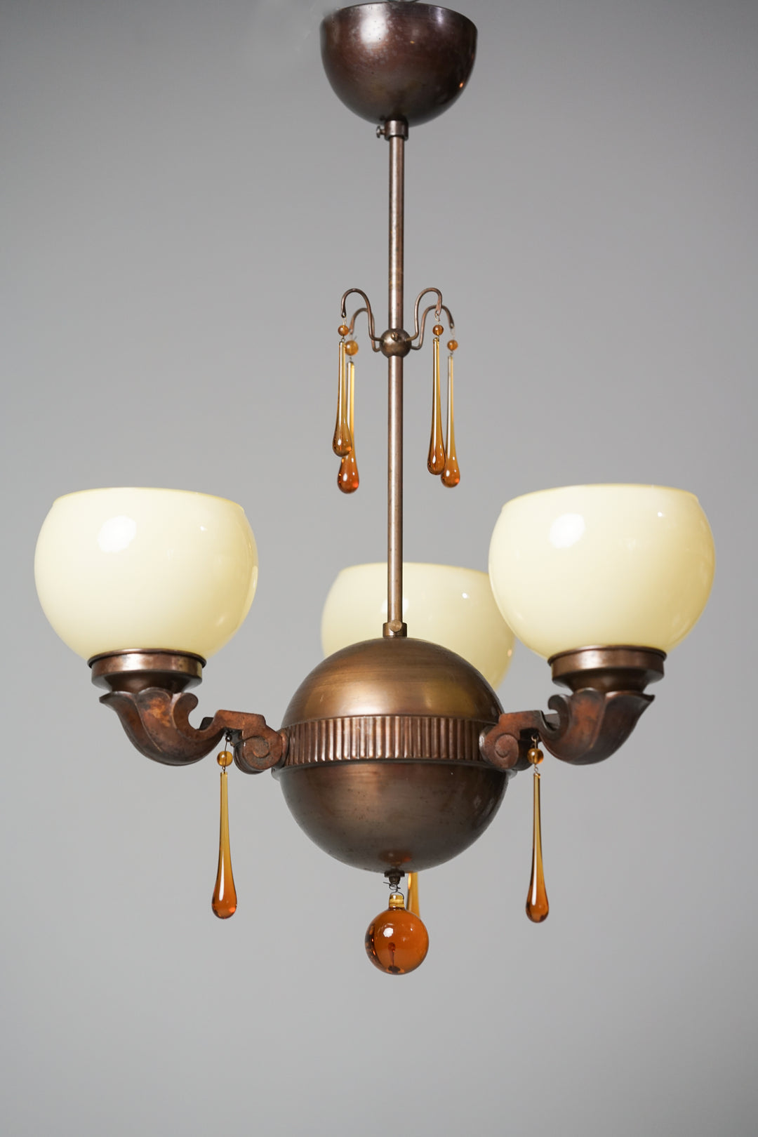 Ceiling light with brass frame. The ceiling light has a ball central section from which three shafts branch off, supporting natural white glass shades. At the bottom of the ball, on frames that support the glass shades and in the centre, amber-colored orange glass details resembling water droplets.
