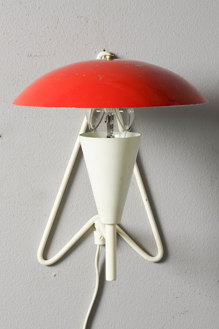 Metal wall lamp. White body, round shade in red painted metal. Triangular wall fixing, body resembles a candle.