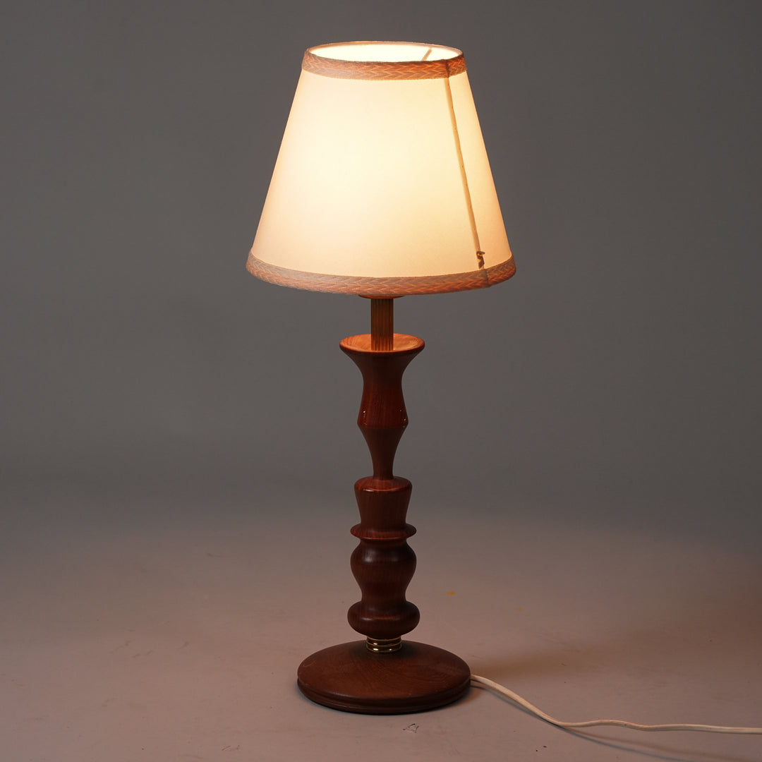 Table lamp with teak frame. Teak frame with circular elements. Brass details on the body. Shade in white fabric with pink edging.