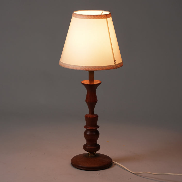 Table lamp with teak frame. Teak frame with circular elements. Brass details on the body. Shade in white fabric with pink edging.