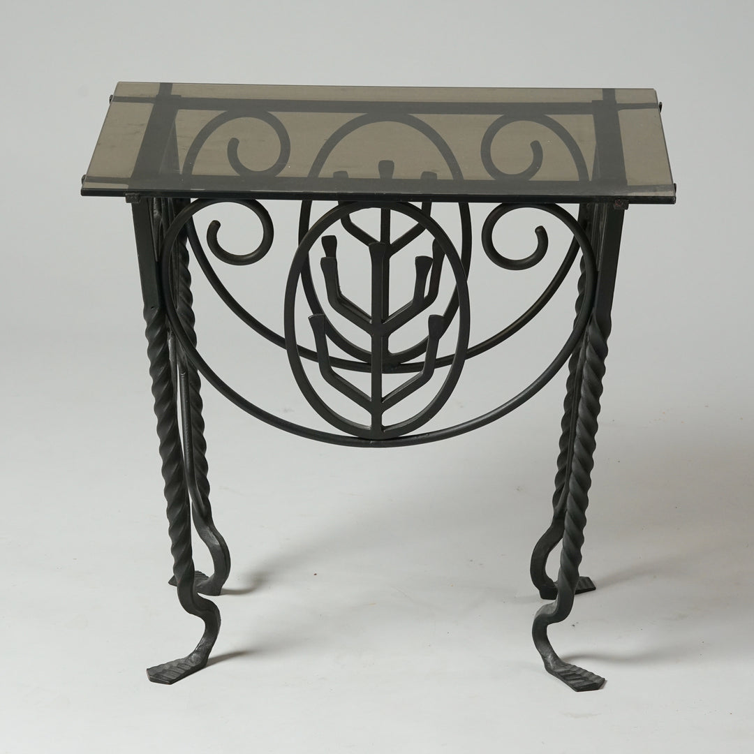 A table with grey glass top. The legs and frame of the table are decorated and made of iron.