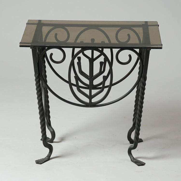 A table with grey glass top. The legs and frame of the table are decorated and made of iron.