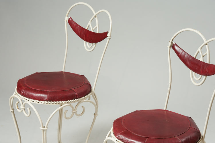 Decorated wrought iron chair painted white with red leather seat and small backrest.