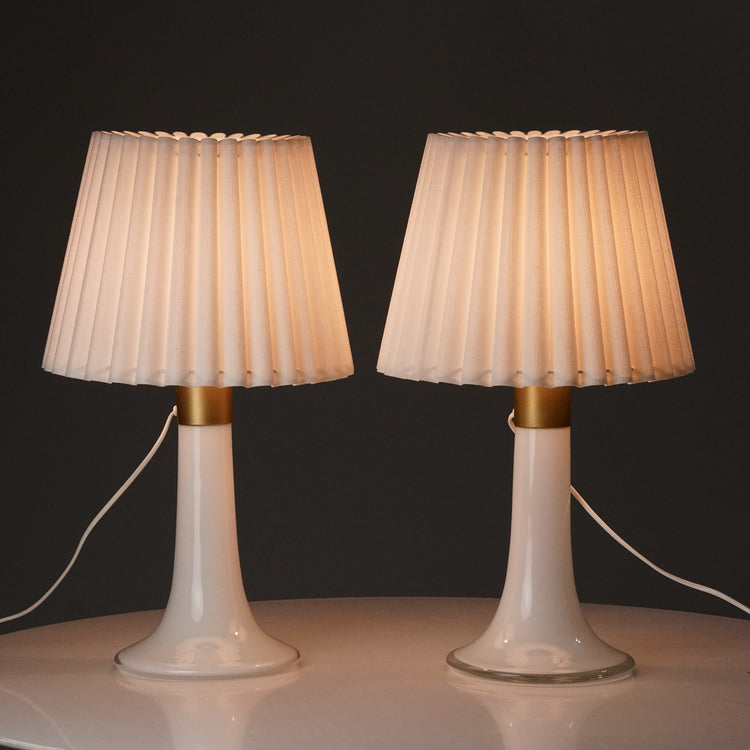 Two lamps with white pleated shades and white glass bases. Has a detail on the base painted with golden color.
