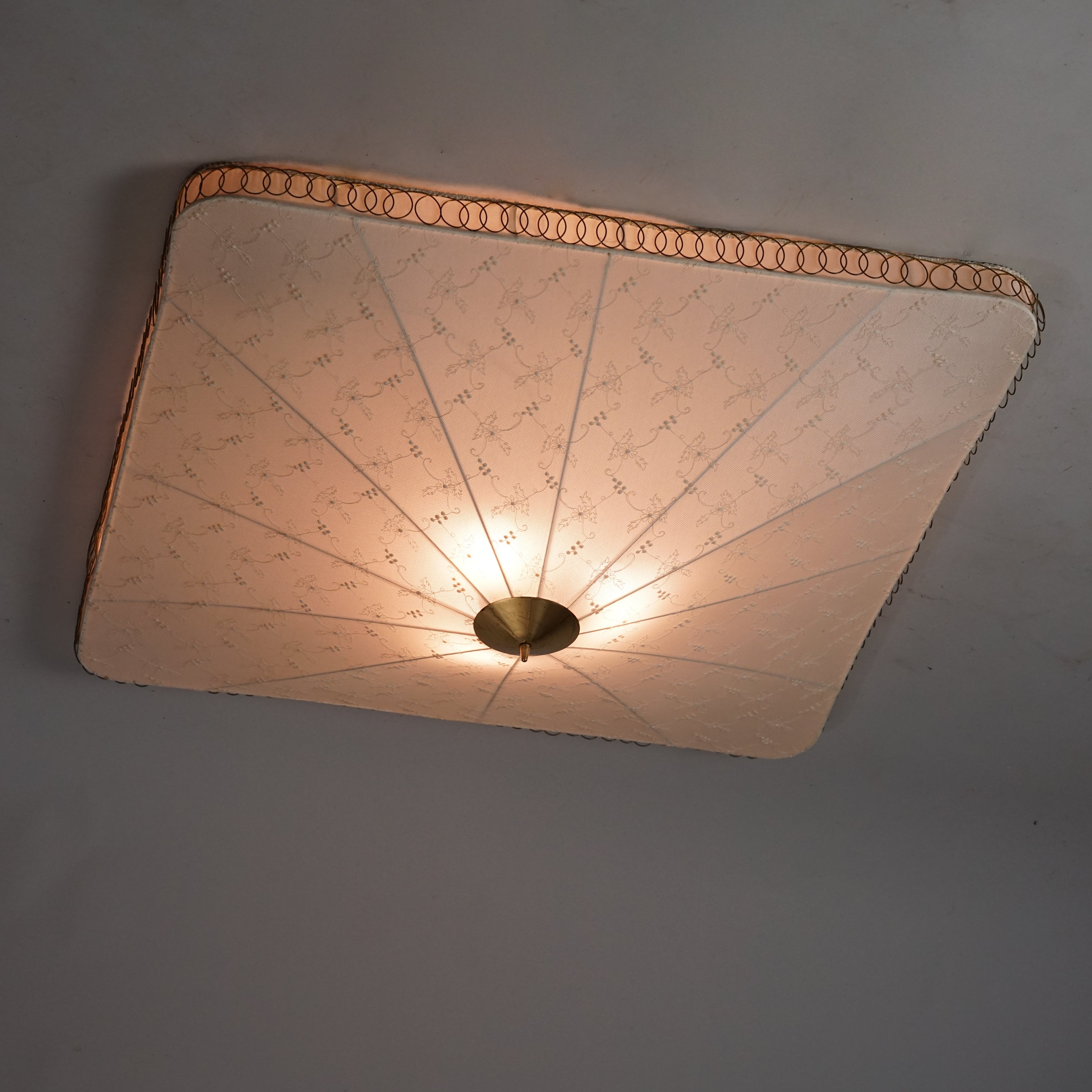 Neliön muotoinen plafondi, jonka silkkivarjostimessa on käsin kirjailtu kukkakuviointi. Valaisimen keskellä ja reunoissa on messinkiyksityiskohdat.