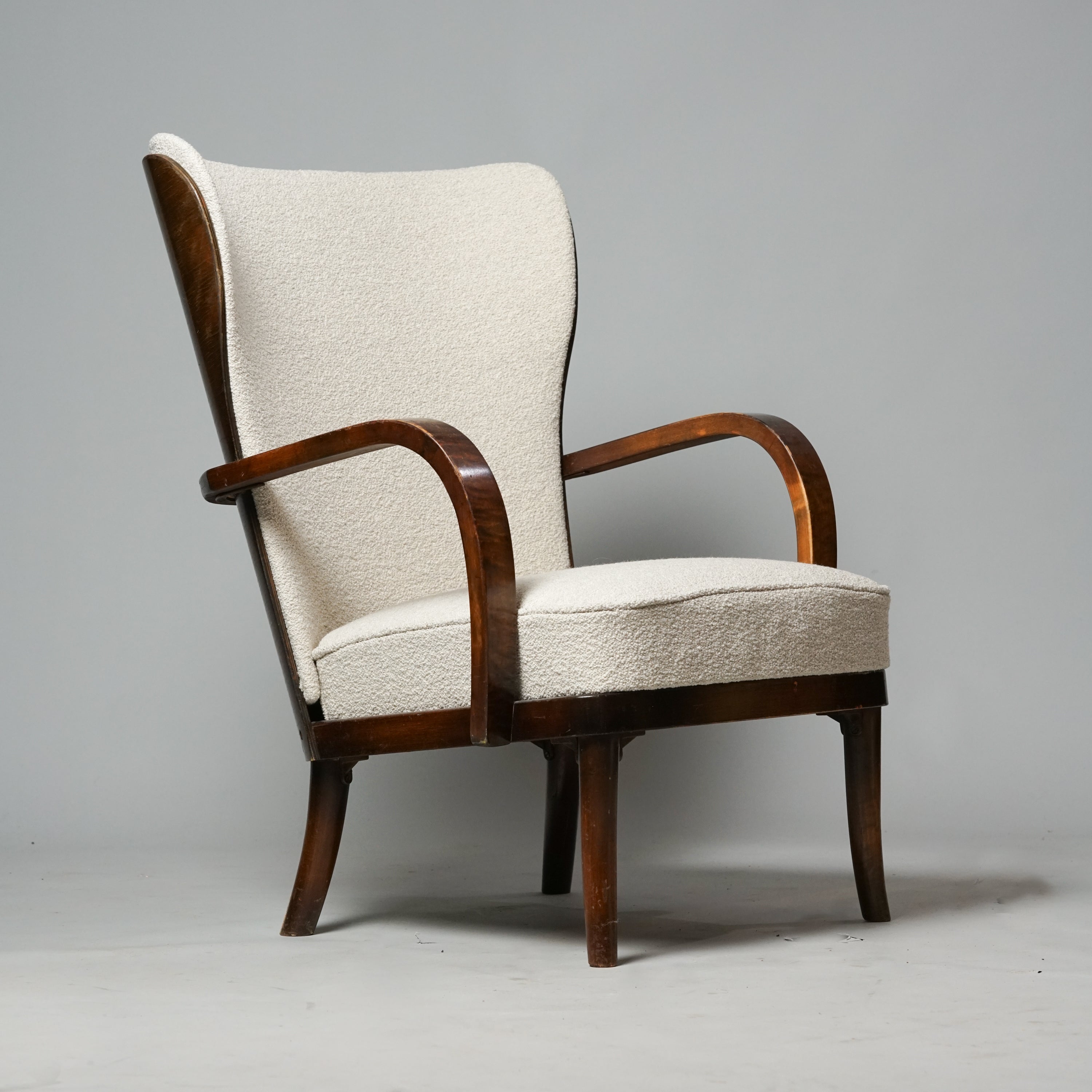 Wingback-tuoli tehty tummasta puusta. Istuinosa on verhoiltu vaalealla kankaalla.