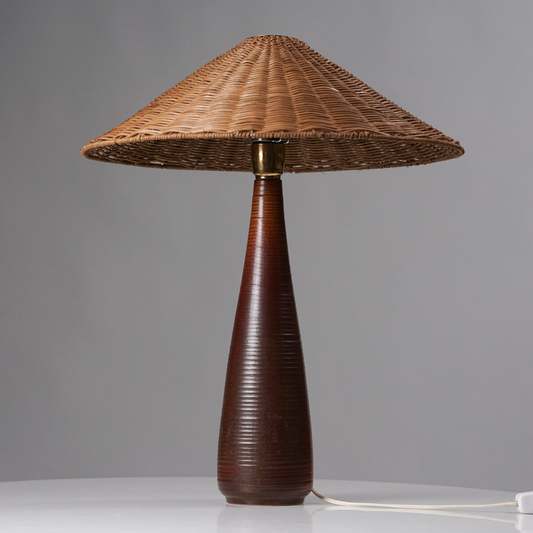 Table lamp that has a woven shade and brown base.