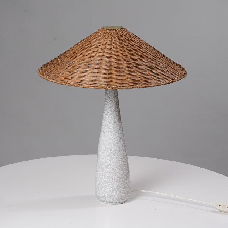 Table lamp that has a woven shade and white base with a marble pattern.