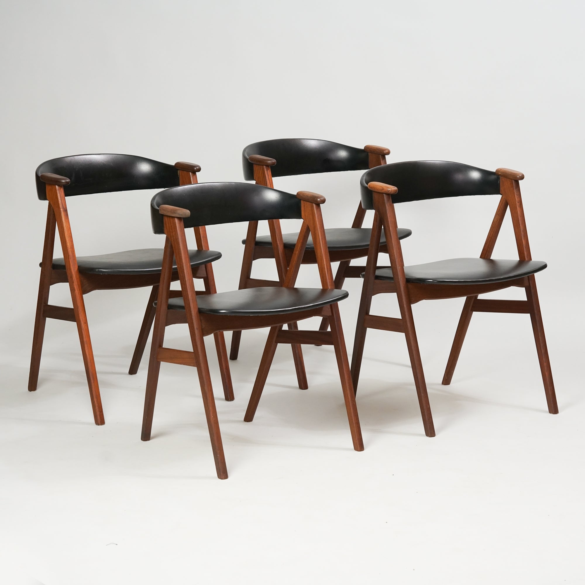 neljä samanlaista tiikistä tehtyä tuolia, joissa keinonahkaiset istuimet ja selkänojat.