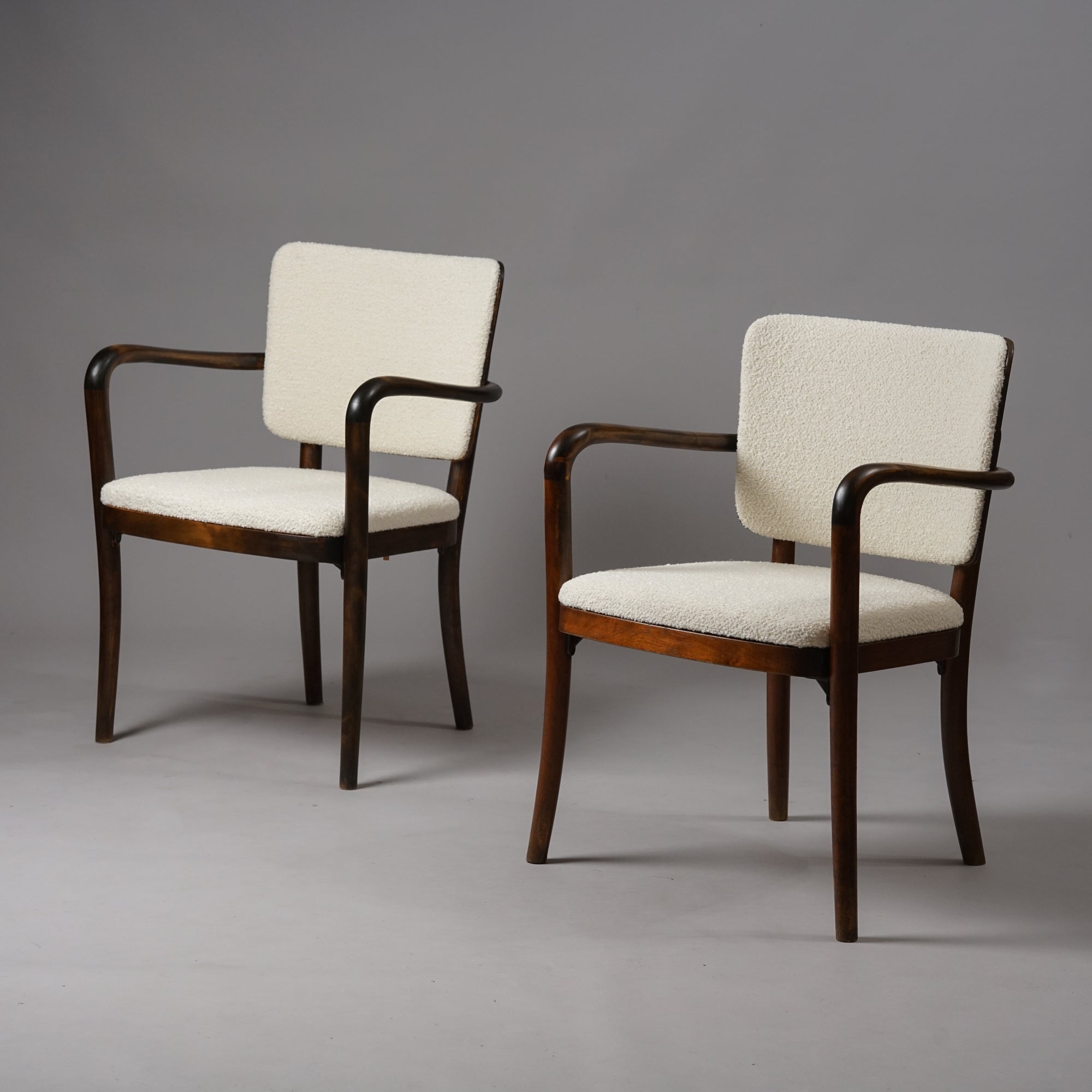 Two identical chairs. The frame of the chair is made of wood and is dark in color, while the seat and backrest has been upholstered in white fabric.