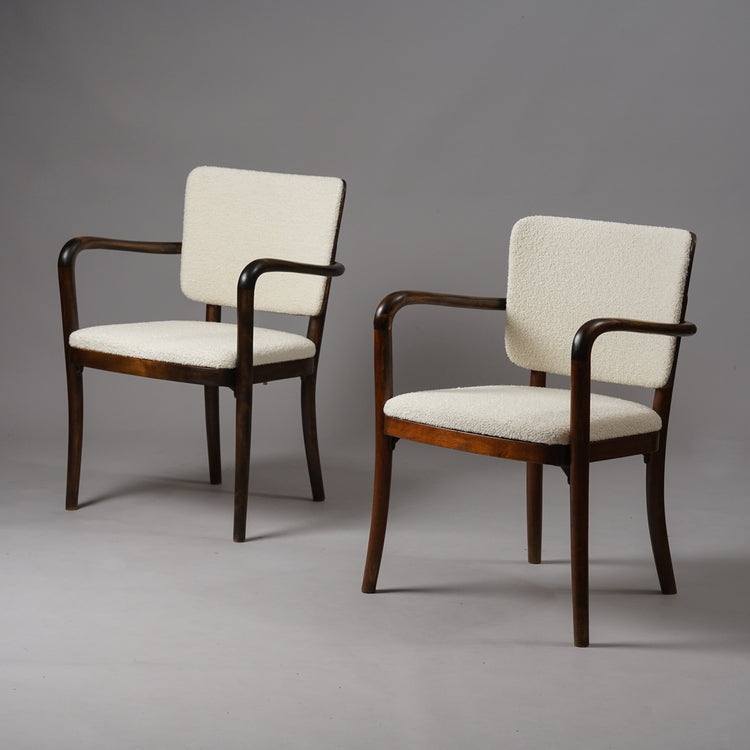 Two identical chairs. The frame of the chair is made of wood and is dark in color, while the seat and backrest has been upholstered in white fabric.