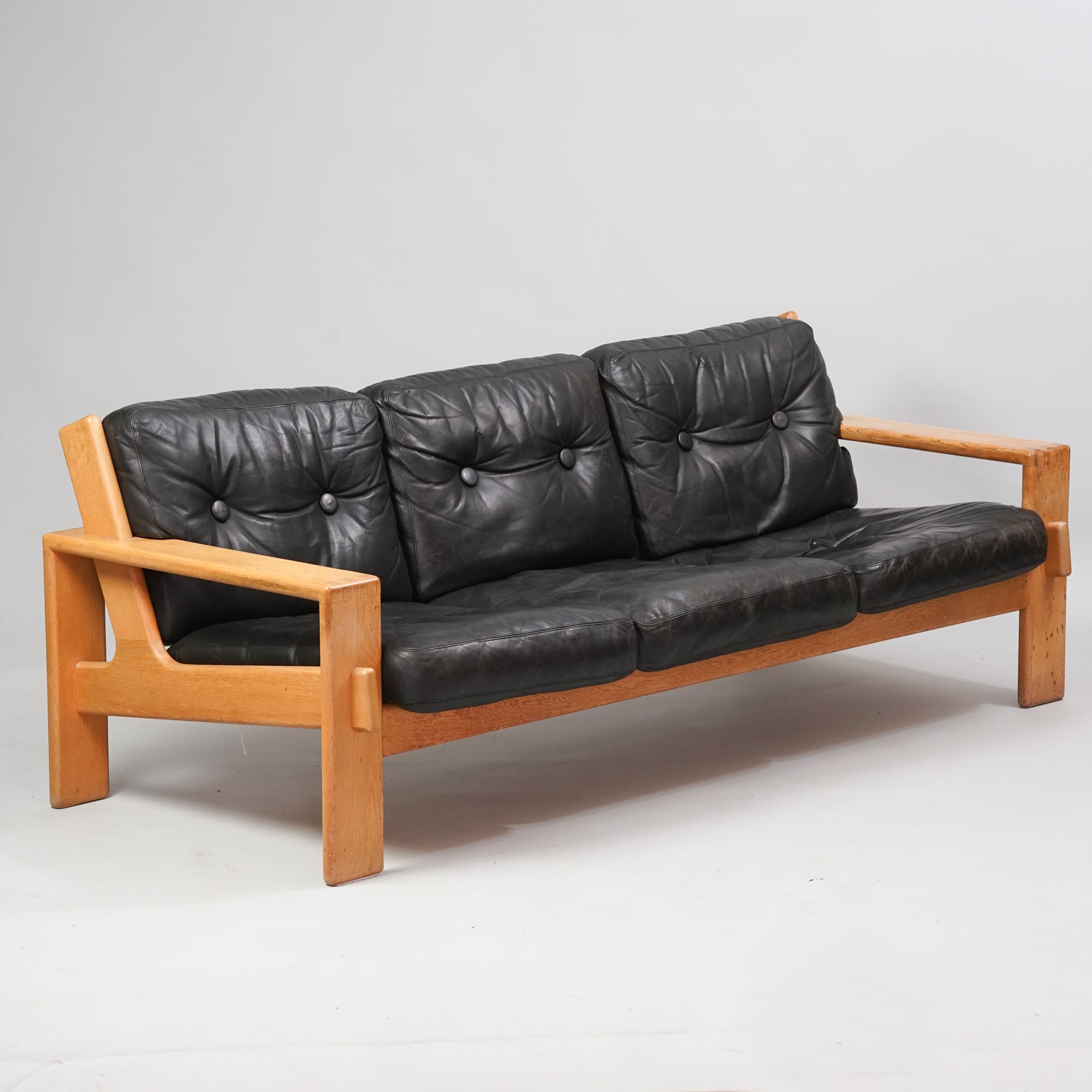 Kolmen istuttava sohva, jonka runko on tammea ja istuin mustaa nahkaa.
