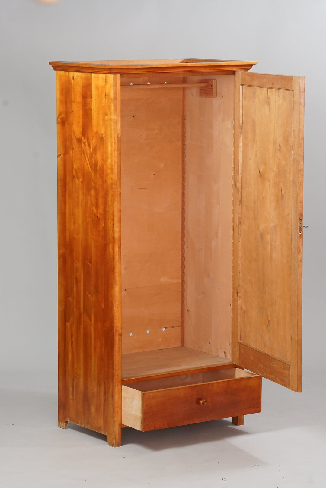Whole birch cabinet with a door and one drawer at the bottom. Inside the cabinet is a rod for hanging clothes off of. 