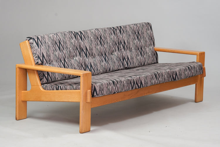 A coffee table made of oak with a couch and two armchairs that have oak frames. The fabric on the couch and armchairs is a zigzag - pattern.