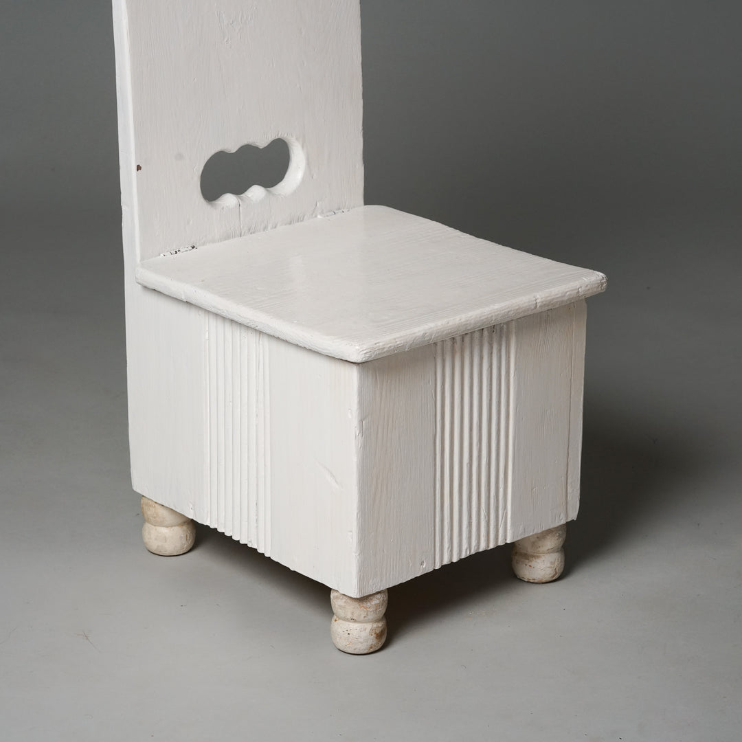 A white children's chair made of wood with a seat that can be opened.