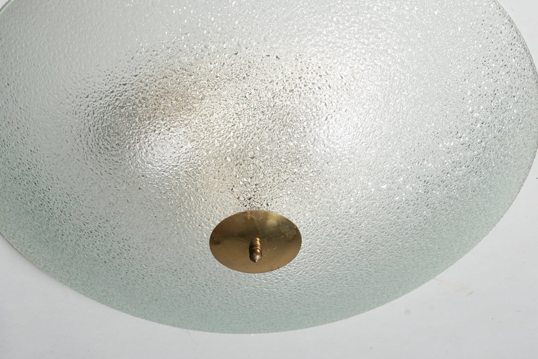 A round plafond made of frosted glass with a brass detailing in the middle.