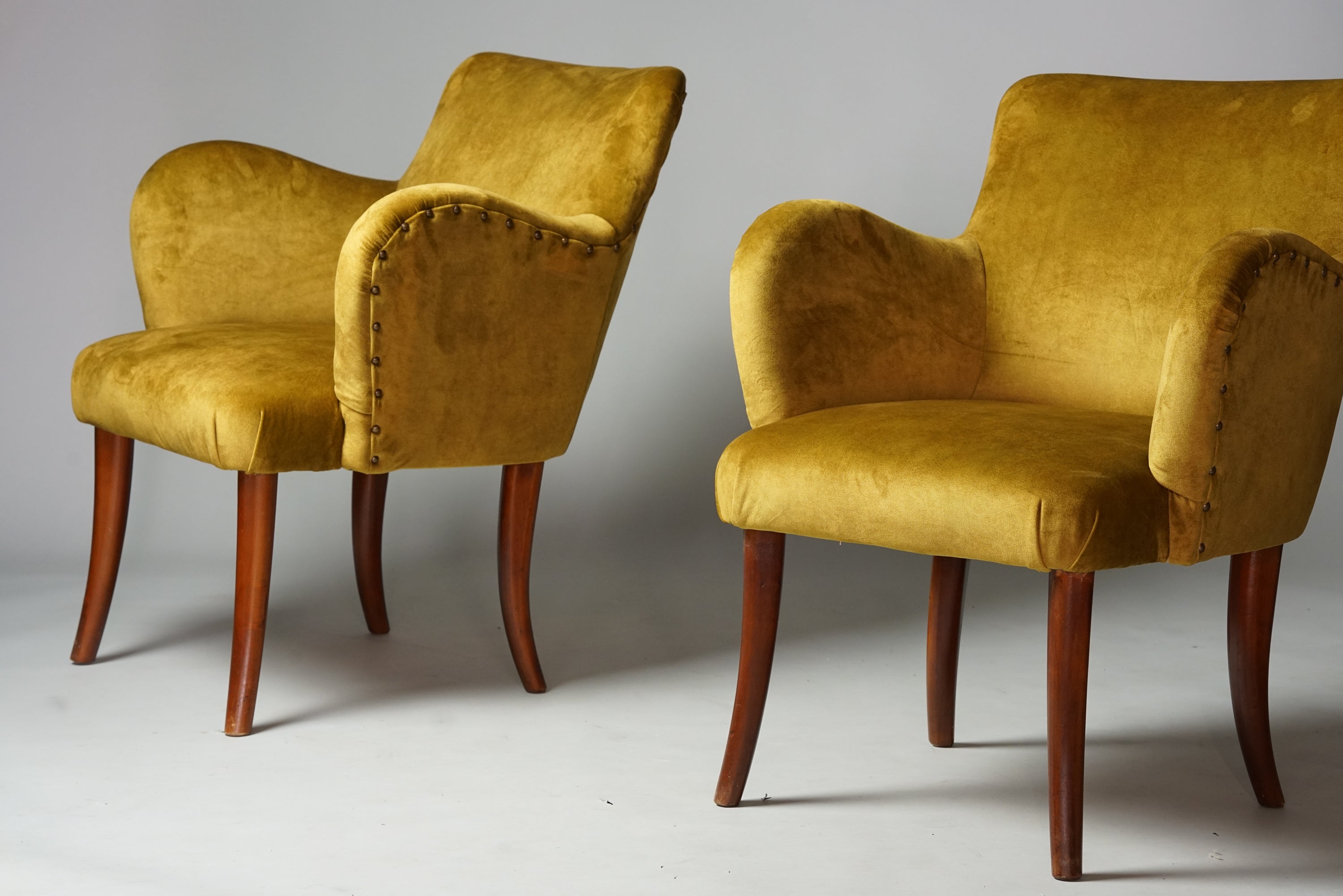 two similar armchairs upholstered in yellow plush fabric. The legs are stained birch and the armrests are decorated. 