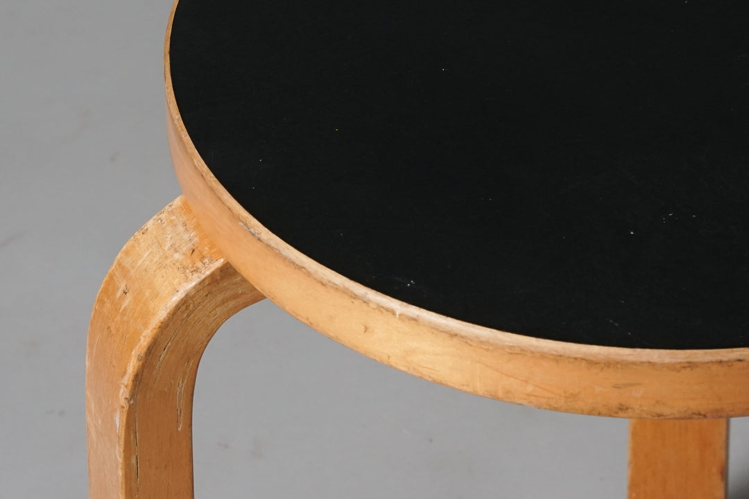 Round stool with black seat and three honey-coloured birch legs.