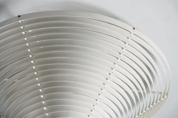 Two metallic white roof lights. The body of the luminaires consists of metal rings decreasing from top to bottom. The bottom of the luminaire is made of blue folding glass.