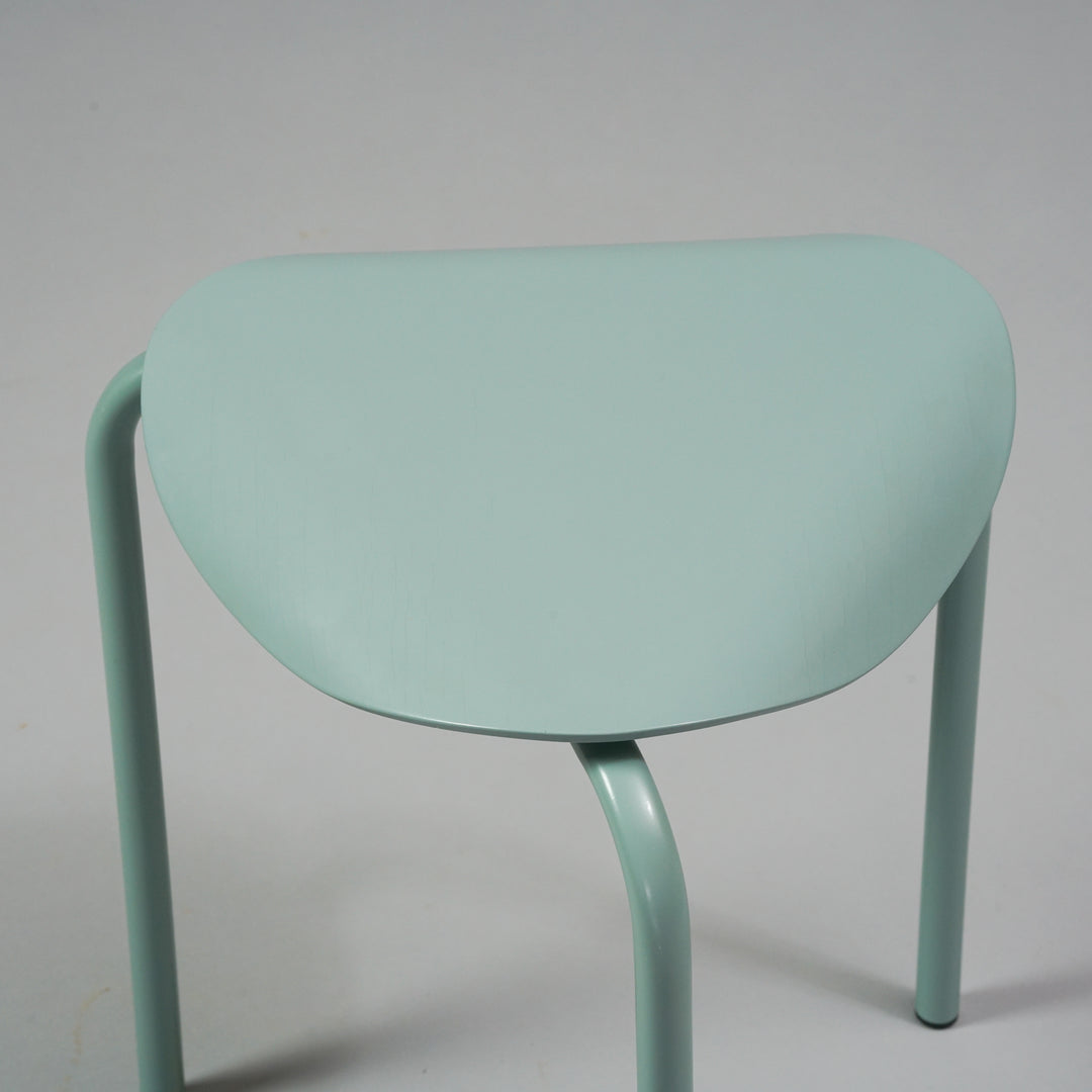 Three legged stool with the edges of the seat bending downwards. Color of the stool is light blue.