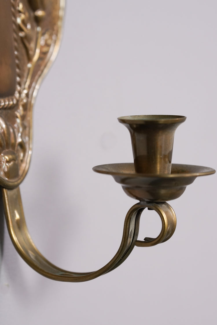 Brass wall sconce with flower inspired decoration and one holder.