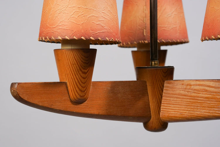 A wooden-framed chandelier with three lights, adorned with orange lamp shades.
