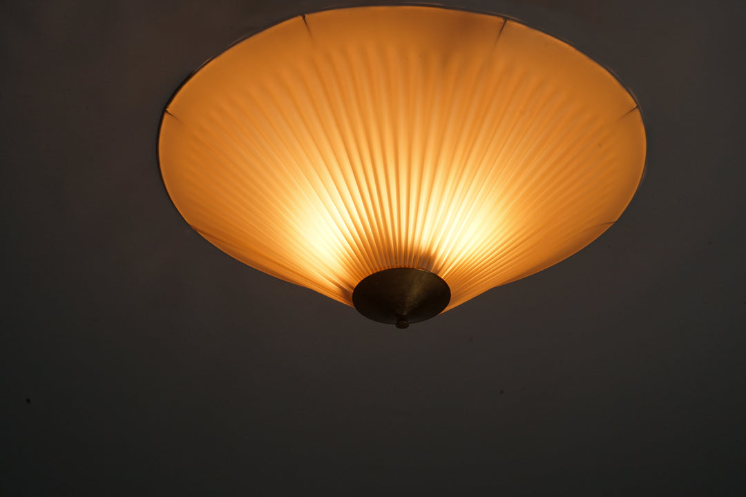 Cone-shaped flush mount. Beige plastic shade. Pleated. Round brass detail in the centre. 