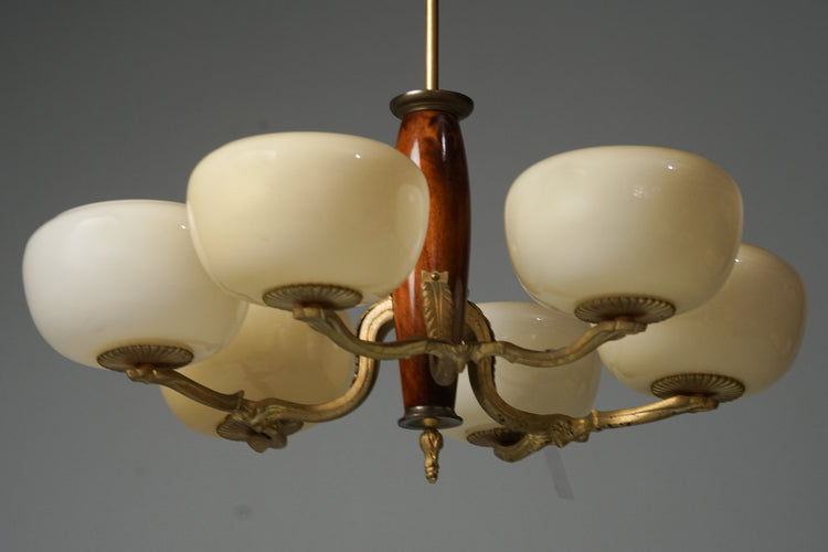 Brass ceiling light. In the centre is a wooden section from which branches a forged iron frame topped by six natural white glass domes. 