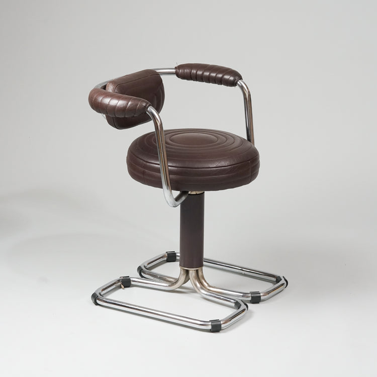 Four identical swivel chairs. The leg consists of two square silver-colored tubes with a leather-covered tubular frame in the middle, which is attached to the seat. The seat is round and in quilted brown leather. The backrest is attached to a tube with armrests. 