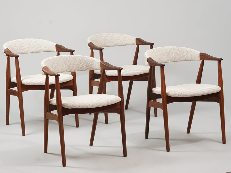 Four identical chairs with four legs. Dark brown teak frame. Backrest and seat in white wool fabric. The backrest is crescent-shaped and floats together with the armrests, which are attached to the frame. 