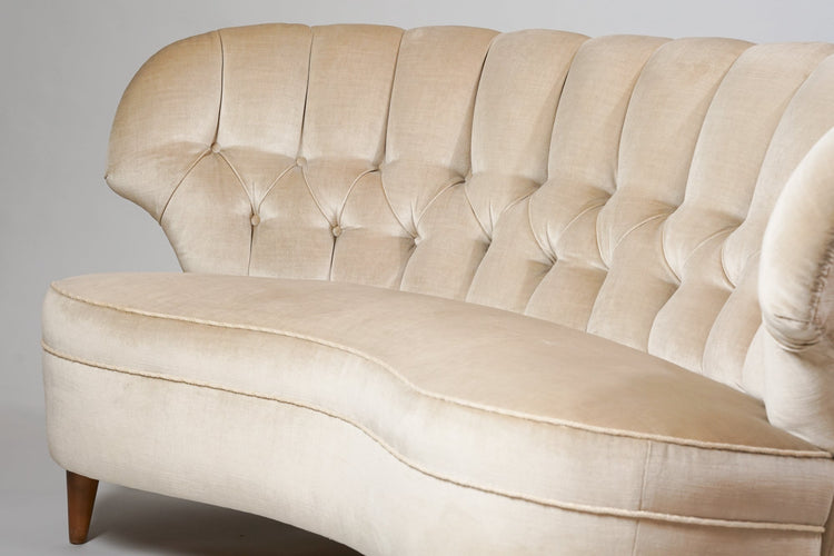 Curved couch with birch legs. The couch has a cream colored plush fabric.
