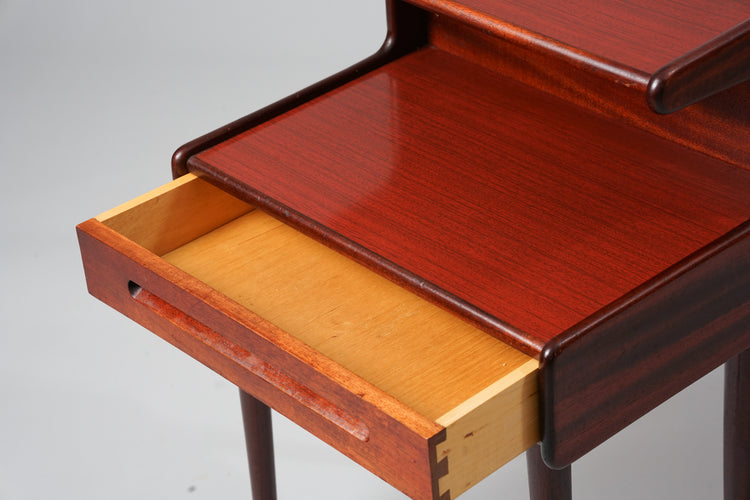 Wooden nightstand with a drawer and two tops. The color of the wood is reddish. 