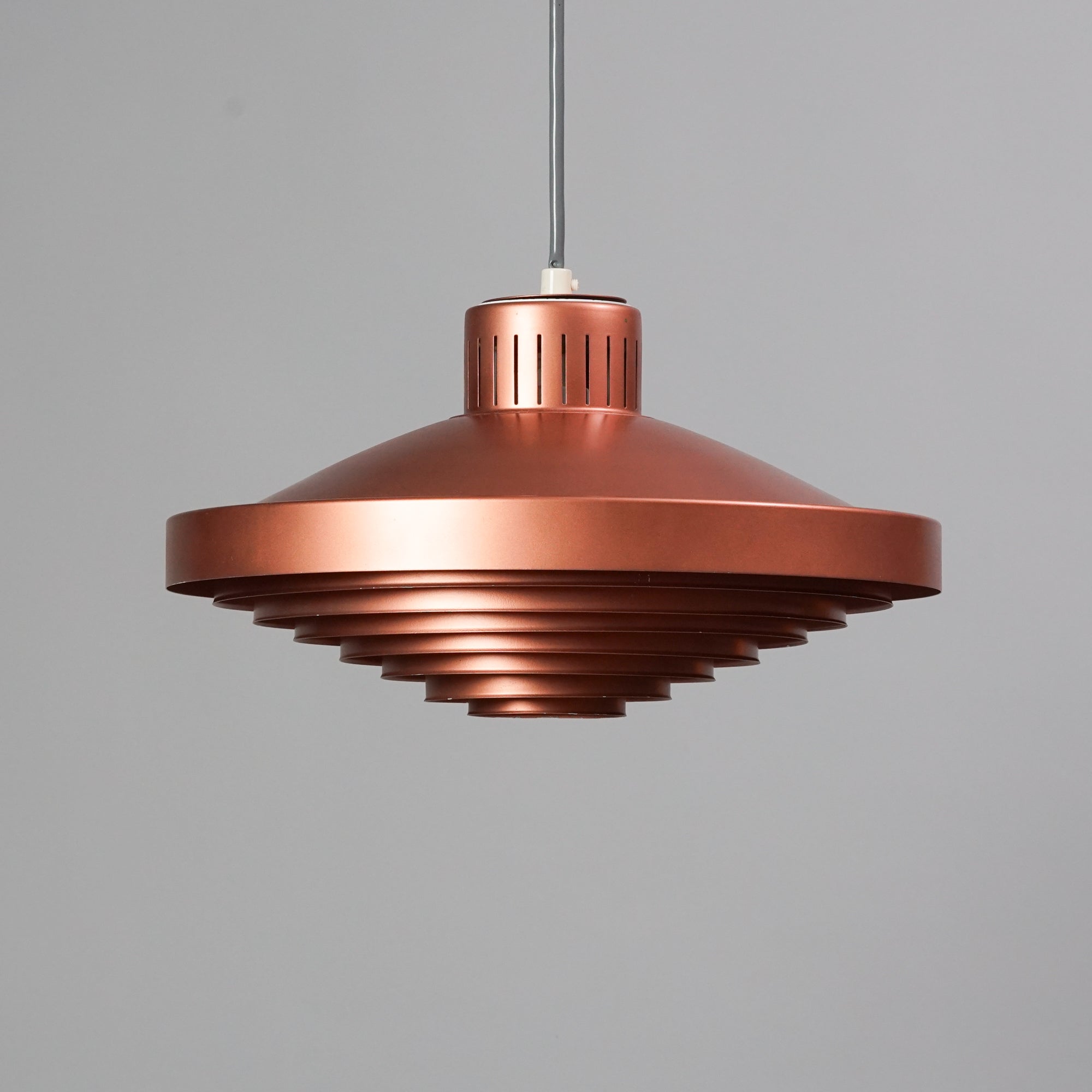 Lamp made of painted metal, with the middle being the widest part. The bottom side of the lamp has a metal grid. Copper color.