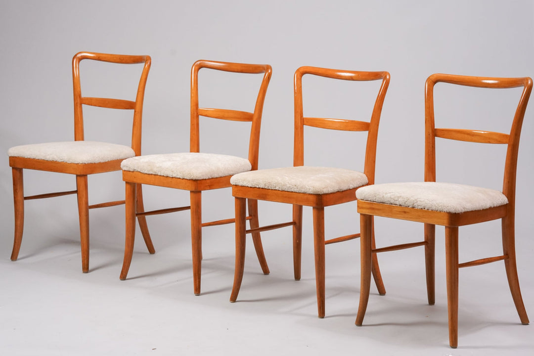 Four identical chairs. Light brown beech frame. Seat in off-white sheep's wool. Four legs on the chairs. The backrest and between the legs of the chair have a crosspiece. 