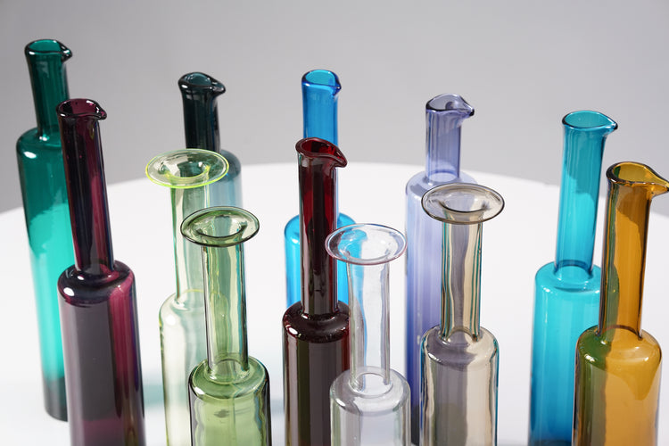 Collection of different colored bottles. Eight of the bottles have pouring lips. The colors are the following colors: Turquoise, Purple, smoky blue, yellowish, green, blue, red, white, brownish, violet, light blue and warm yellow.