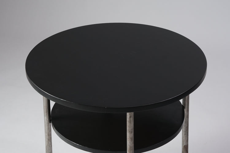 Round coffee table with two tops, both black in color. The legs are made of pipes that connect together under the table.