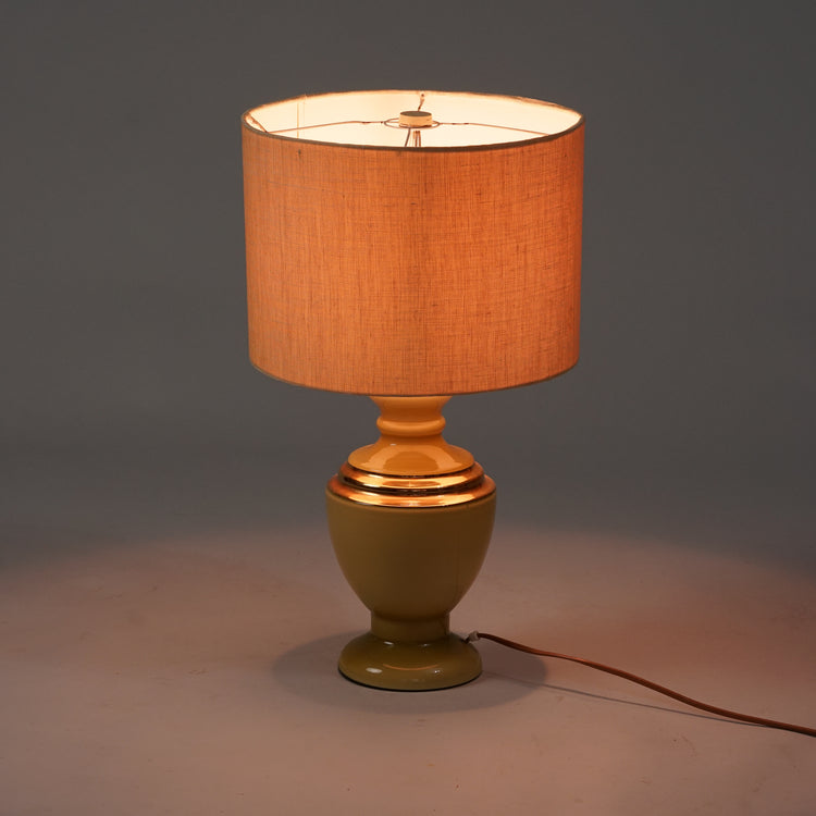 Table lamp with a vase-shaped greenish-yellow body. Glass body. Golden rim on the body. Natural white round shade. 