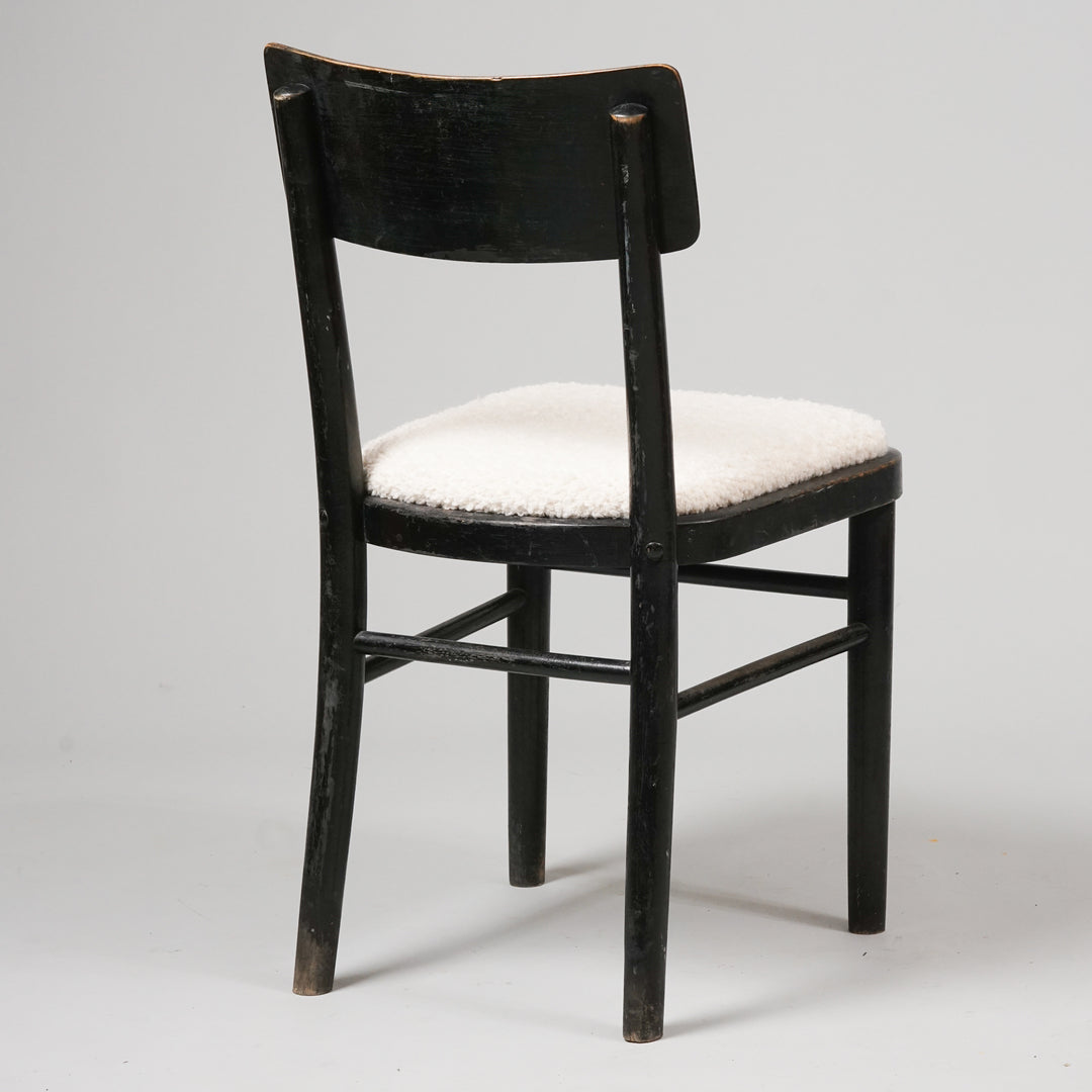 Three identical chairs. Black painted wooden frame. Four legs. Supporting beams between the legs. Seat in white fabric resembling sheep's wool.