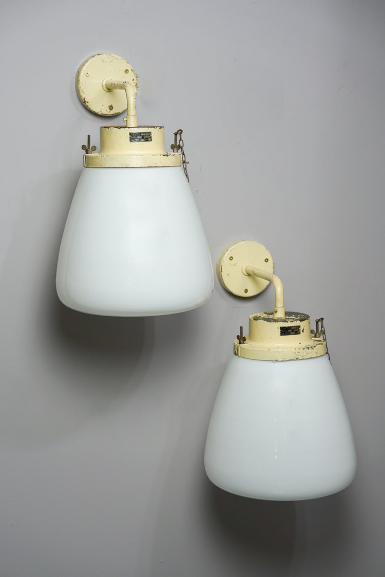 Two identical lamps with white cloudy glass domes that widen at the bottom. The iron frames of the lamps are painted light yellow.