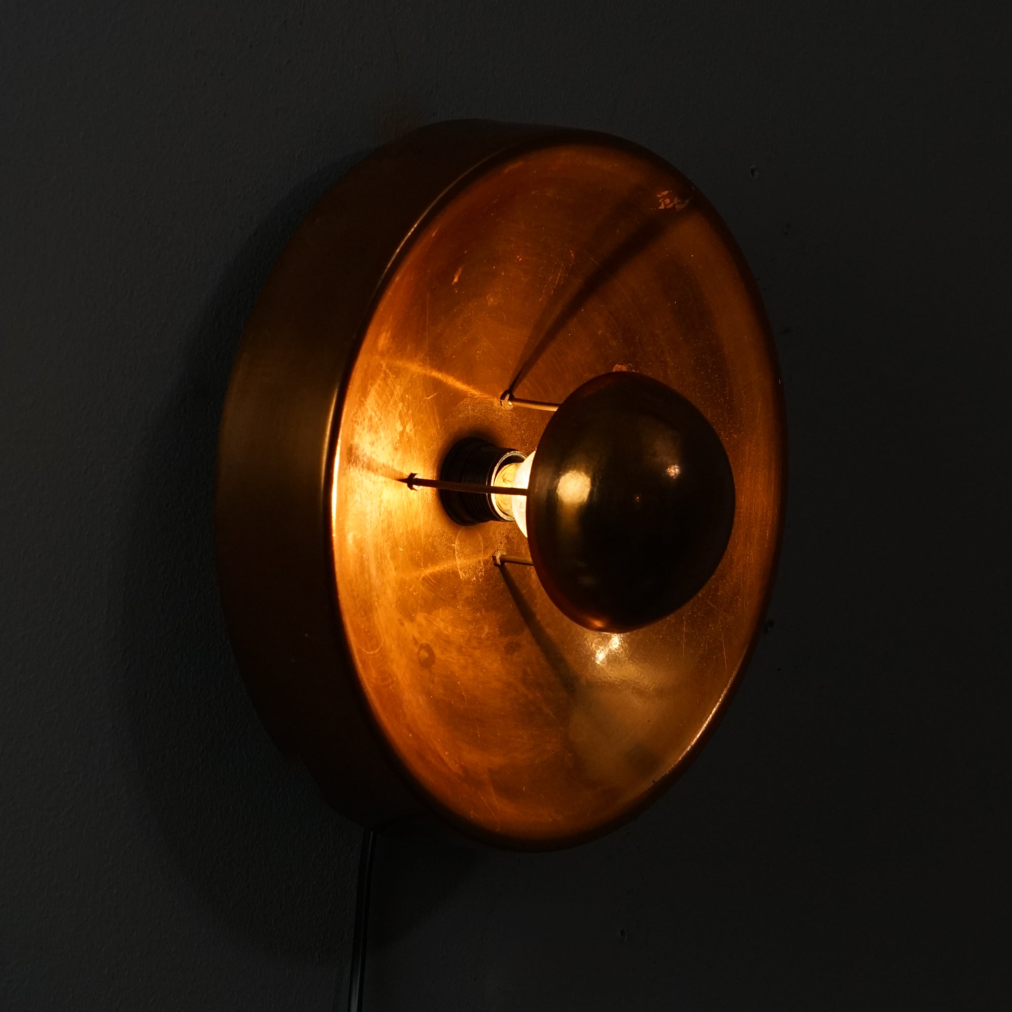 Kuparinen ympyränmuotoinen seinävalaisin, jossa kuparinen kupu lampun edessä.