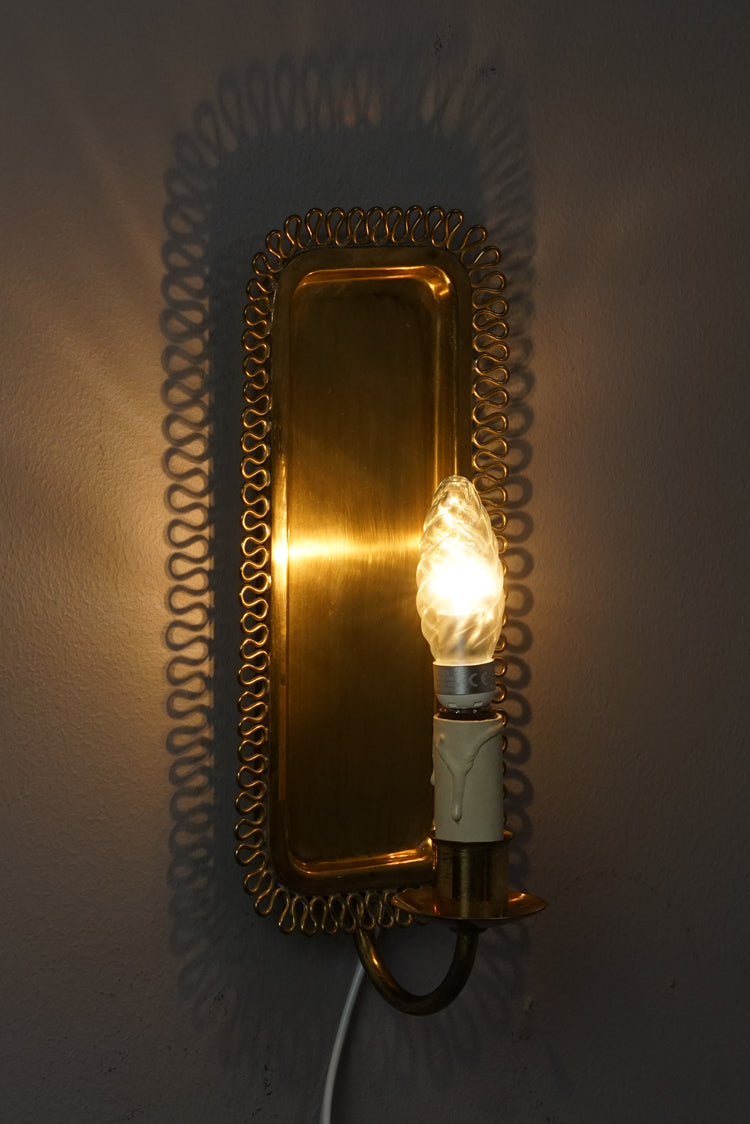 A rectangle sconce made of brass with decorated sides. The holder has a candle detailing, that holds the lamp.