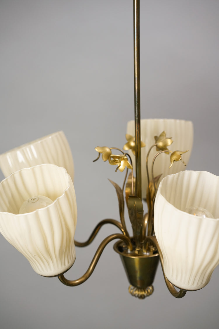 A ceiling lamp with five opal glass domes pointing upwards. The base is made of brass and the lamp has brass flowers decorating it. 