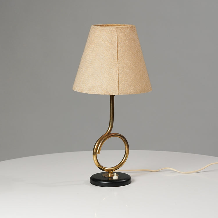Lamp with fabric shade and a brass leg that forms a loop. 