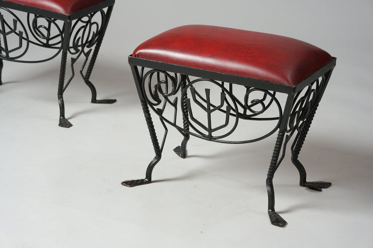 A stool with decorated iron frame and legs. The seat is dark red.