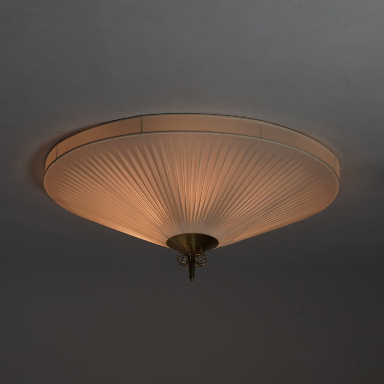 White round plafond with a pleated plastic shade. The lamp has a brass detailing in the middle.