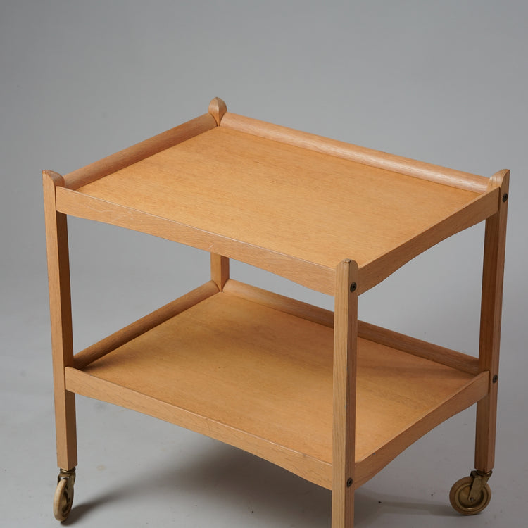 Serving trolley made of oak with two shelves and four wheels.