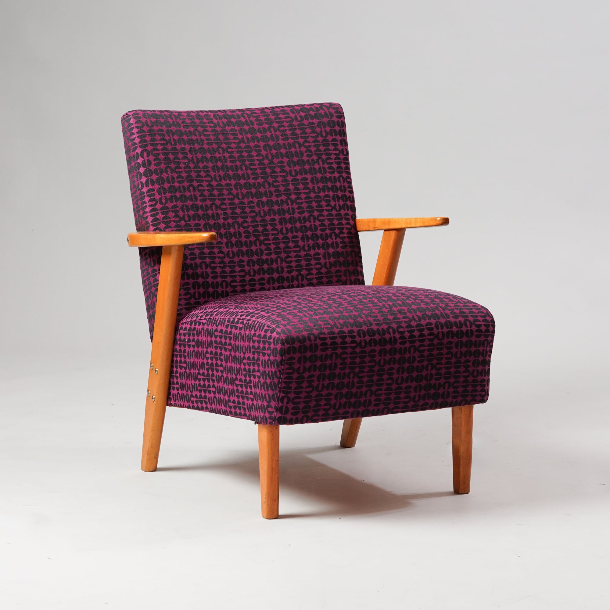 Koivurunkoinen nojatuoli, joka on verhoiltu kuviolliseen violetin ja mustan väriseen kankaaseen.