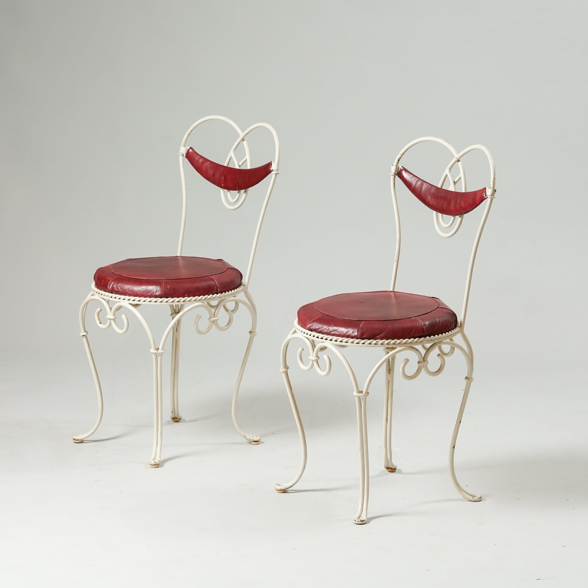 Valkoseksi maalatusta taotusta metallista tehty koristeellinen tuoli, jossa punainen nahkainen istuin ja ohut selkänoja.