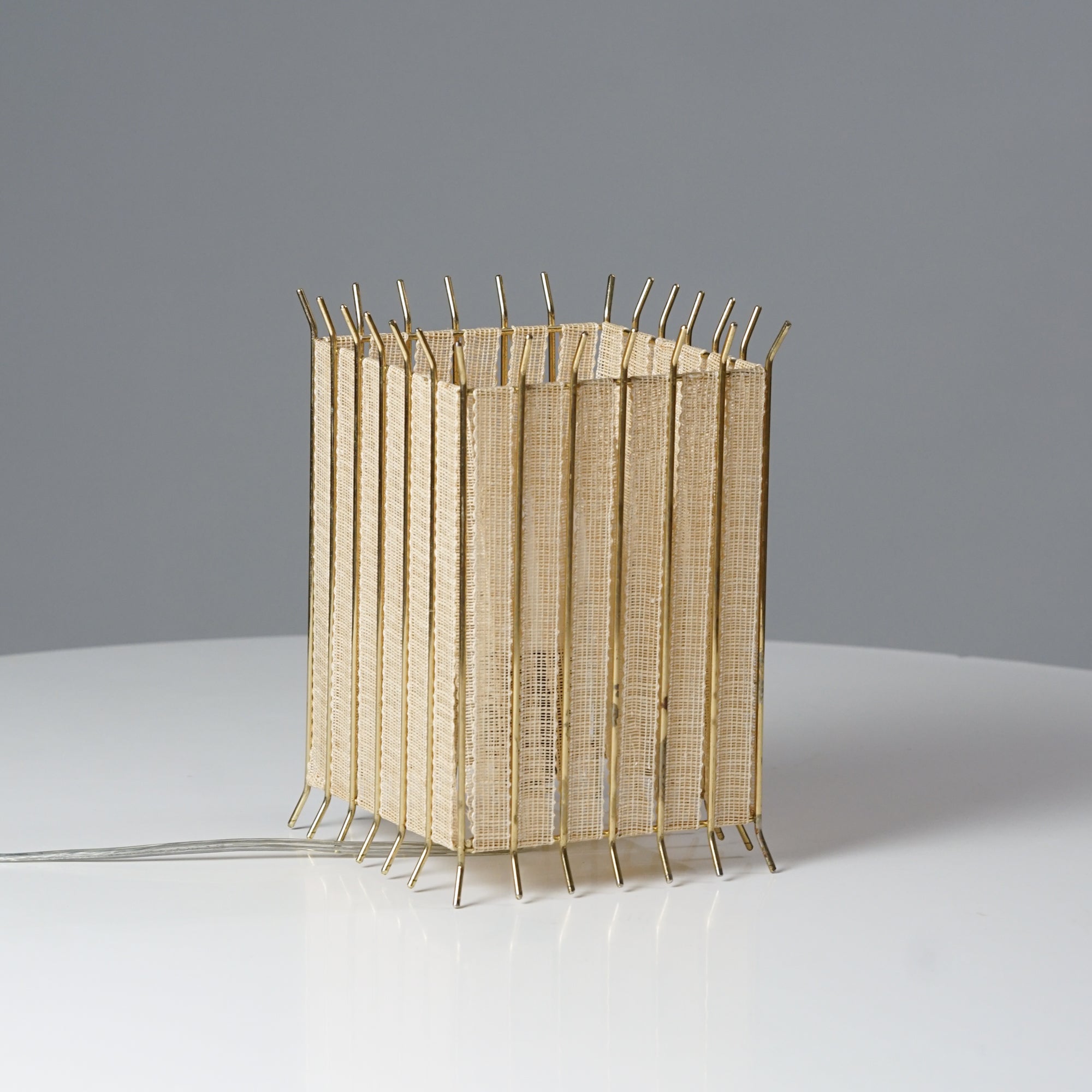 Cube shaped lamp, where the shade is flax and frame brass.